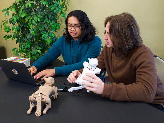 Robotics Projects: Two students working on coding robot cat Nybble and robotic dog prototype at a table.